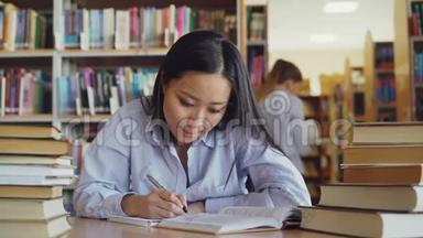 年轻漂亮的亚洲女学生坐在桌子旁，周围是大图书馆里成堆的书，从大图书馆改写课文